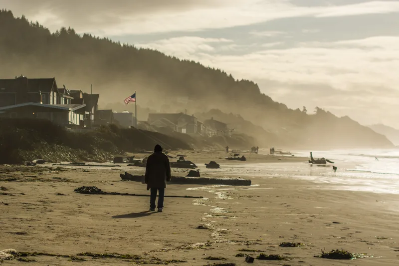 A single figure walking along a wide empty beach under an overcast sky